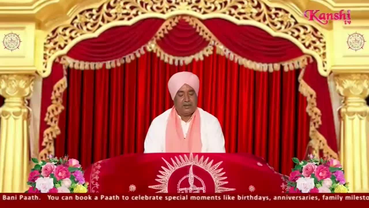 A man in a pink turban and white robe sits behind a red table, speaking. The Kanshi TV logo is visible in the upper right corner, and the backdrop is a deep red curtain.
A man in a pink turban and white robe sits behind a red table, speaking. The Kanshi TV logo is visible in the upper right corner, and the backdrop is a deep red curtain.