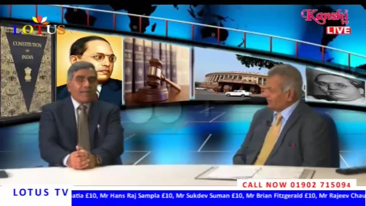 Two men in suits sit at a desk on a Kanshi TV set, with images of Indian legal and political figures displayed behind them. The Lotus TV logo and a call-in number are visible in the lower portion of the screen.
