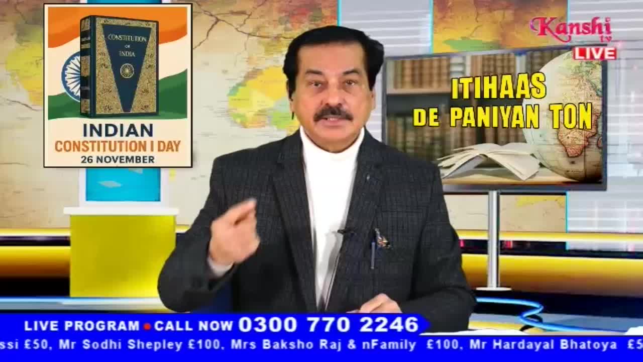 A man in a dark suit is gesturing emphatically, speaking on Kanshi TV. Behind him, a screen displays the words "ITIHAAS DE PANIYAN TON" and a globe, while a graphic commemorates Indian Constitution Day.
