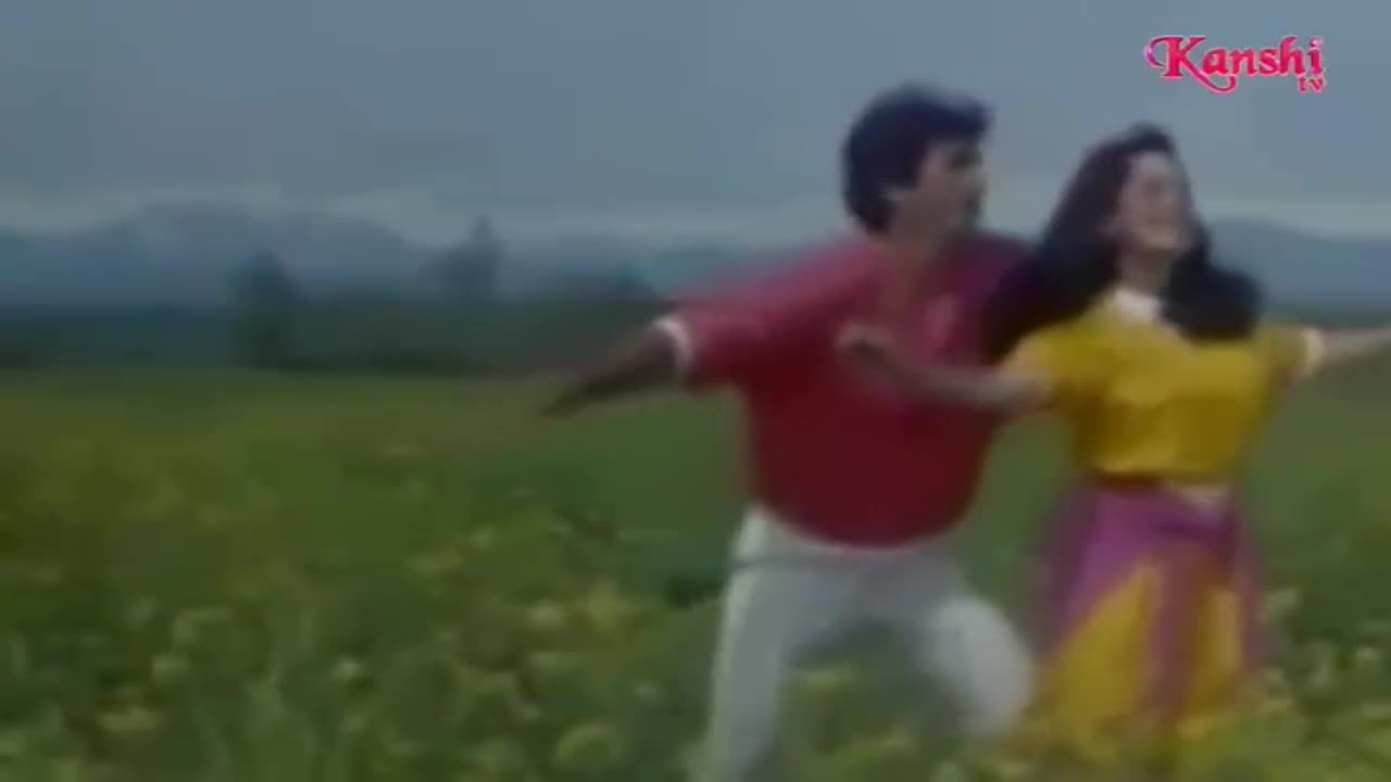A man in a red shirt and a woman in yellow and pink twirl in a field, arms outstretched. The Kanshi TV logo is visible in the corner, broadcasting from the United Kingdom.
