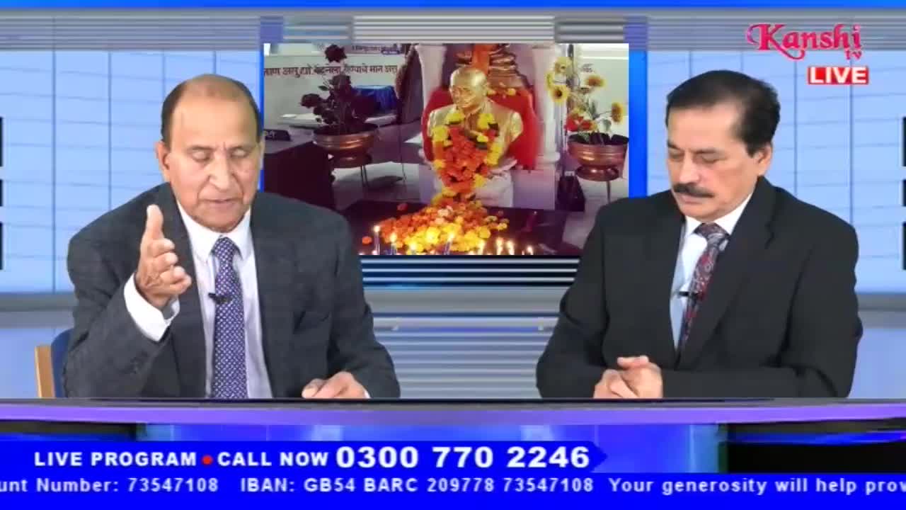 On Kanshi TV, two men in suits sit at a desk. The man on the left gestures with his hand as he speaks, while a backdrop shows a statue adorned with flowers.
On Kanshi TV, two men in suits sit at a desk. The man on the left gestures with his hand as he speaks, while a backdrop shows a statue adorned with flowers.