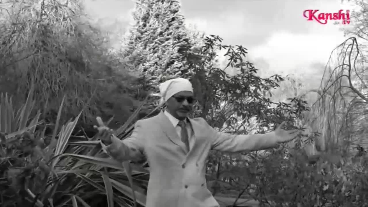 A man in a light suit and turban stands with his arms outstretched, gesturing towards the lush greenery of an English garden. The Kanshi TV logo appears in the top right corner.