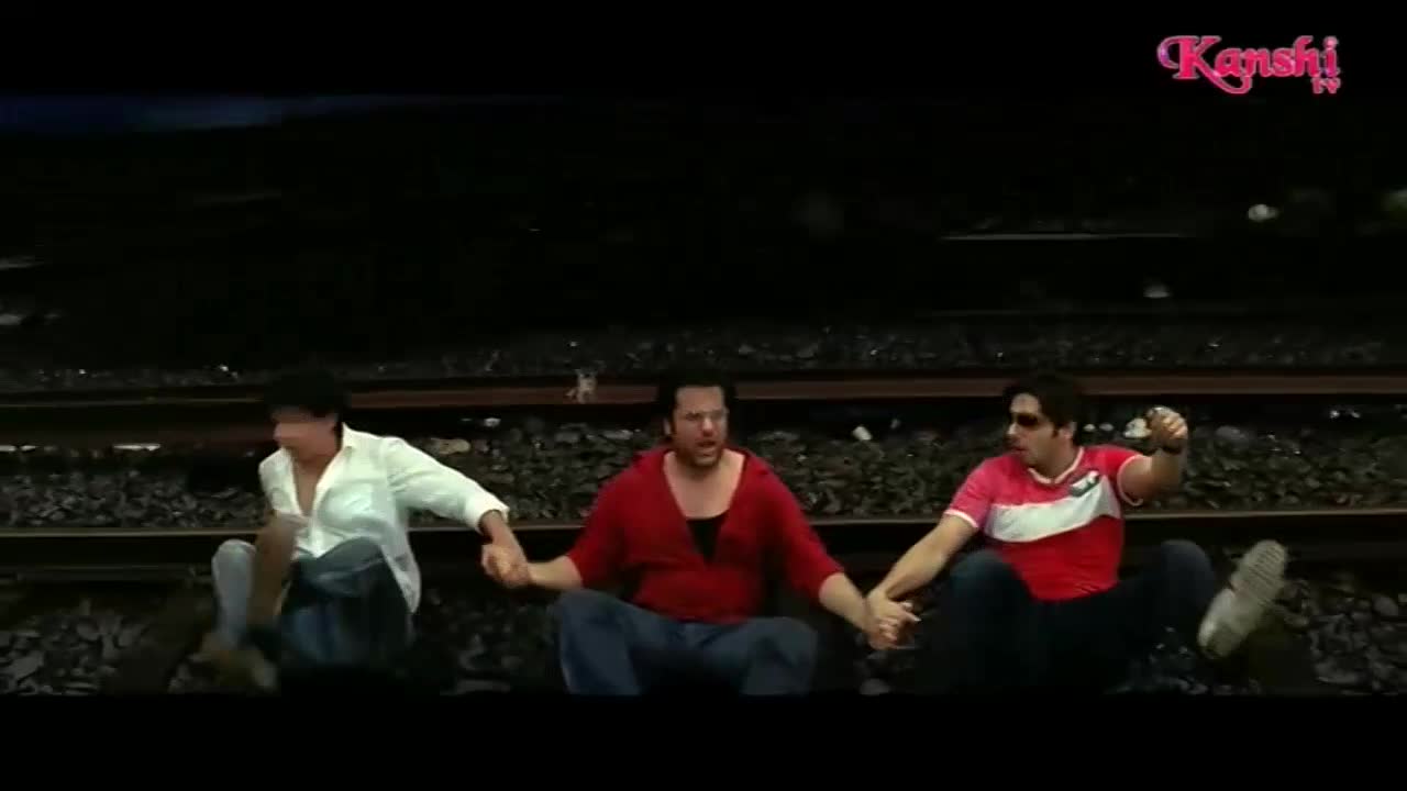 Three men sit on train tracks, holding hands. The Kanshi TV logo appears in the top right corner.