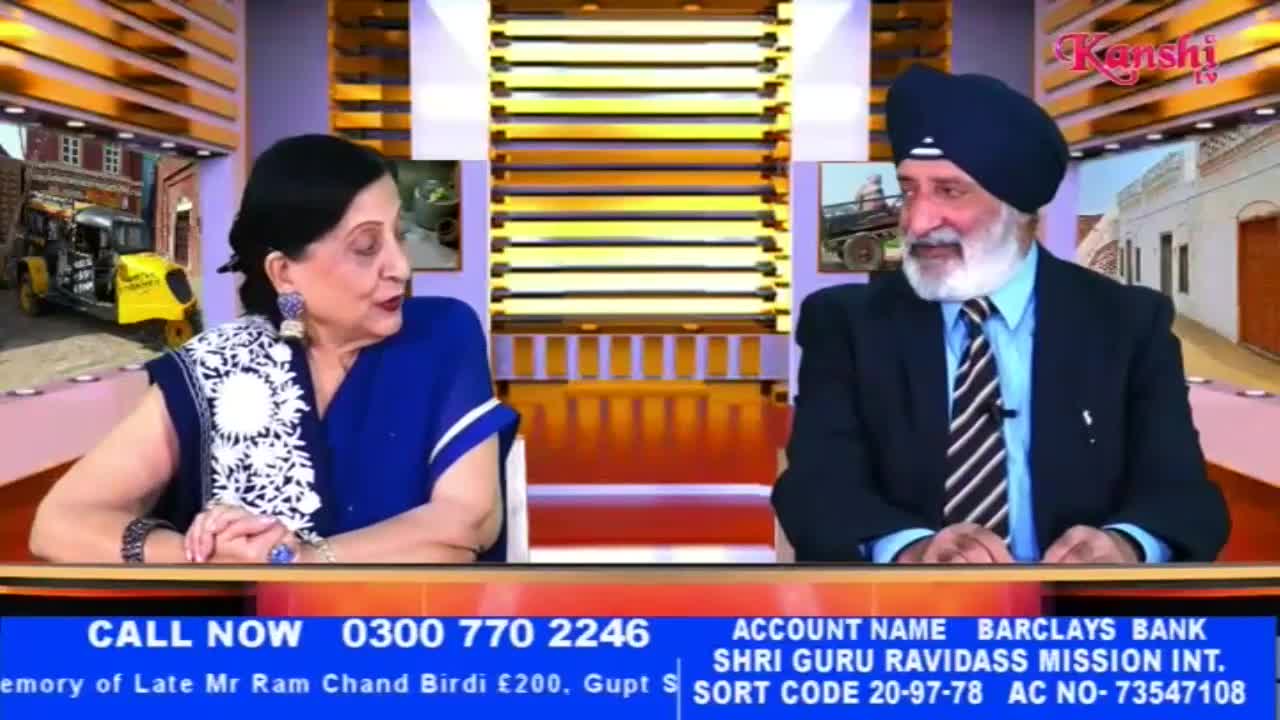 A woman in a blue sari and a man in a suit and turban sit at a desk, facing each other. The Kanshi TV logo is visible in the upper right corner.