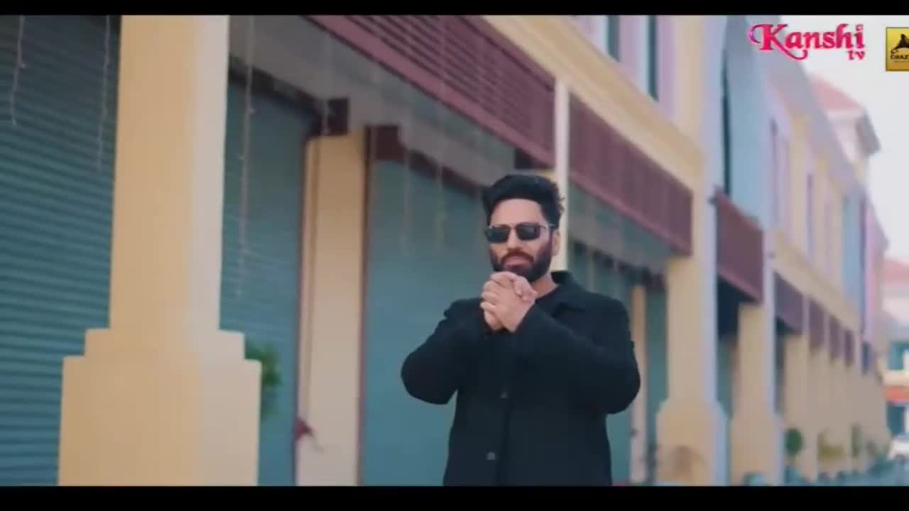 A man in a black coat and sunglasses stands with his hands clasped. The Kanshi TV logo appears in the corner of the screen.