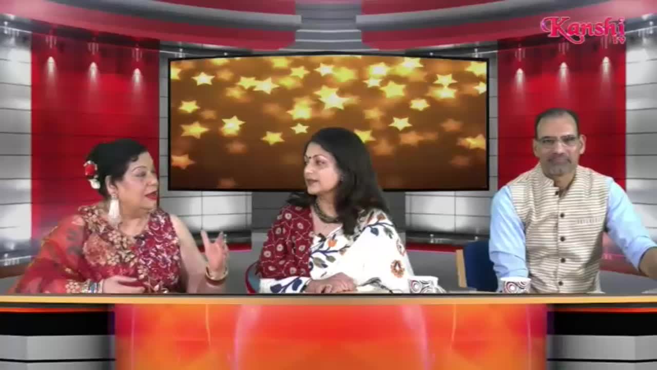Three people sit behind a desk, bathed in the warm glow of a screen displaying scattered golden stars. A woman on the left gestures with her hands as she speaks, while the woman next to her listens intently. A man on the right, wearing a striped vest, looks towards the camera.