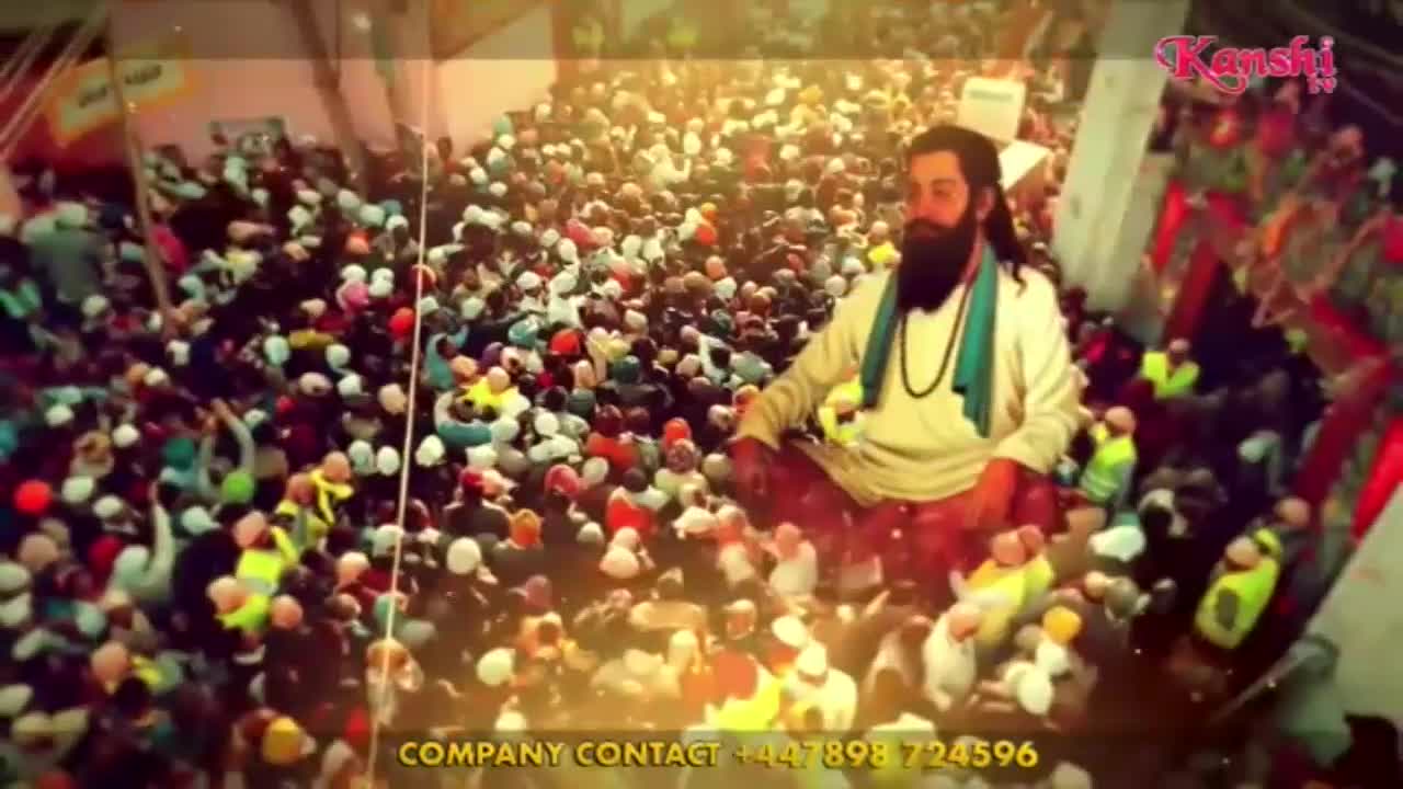 A man with a long beard, wearing a white robe and a teal scarf, sits amidst a vast crowd. People in the throng hold up balloons, their faces turned towards the man.