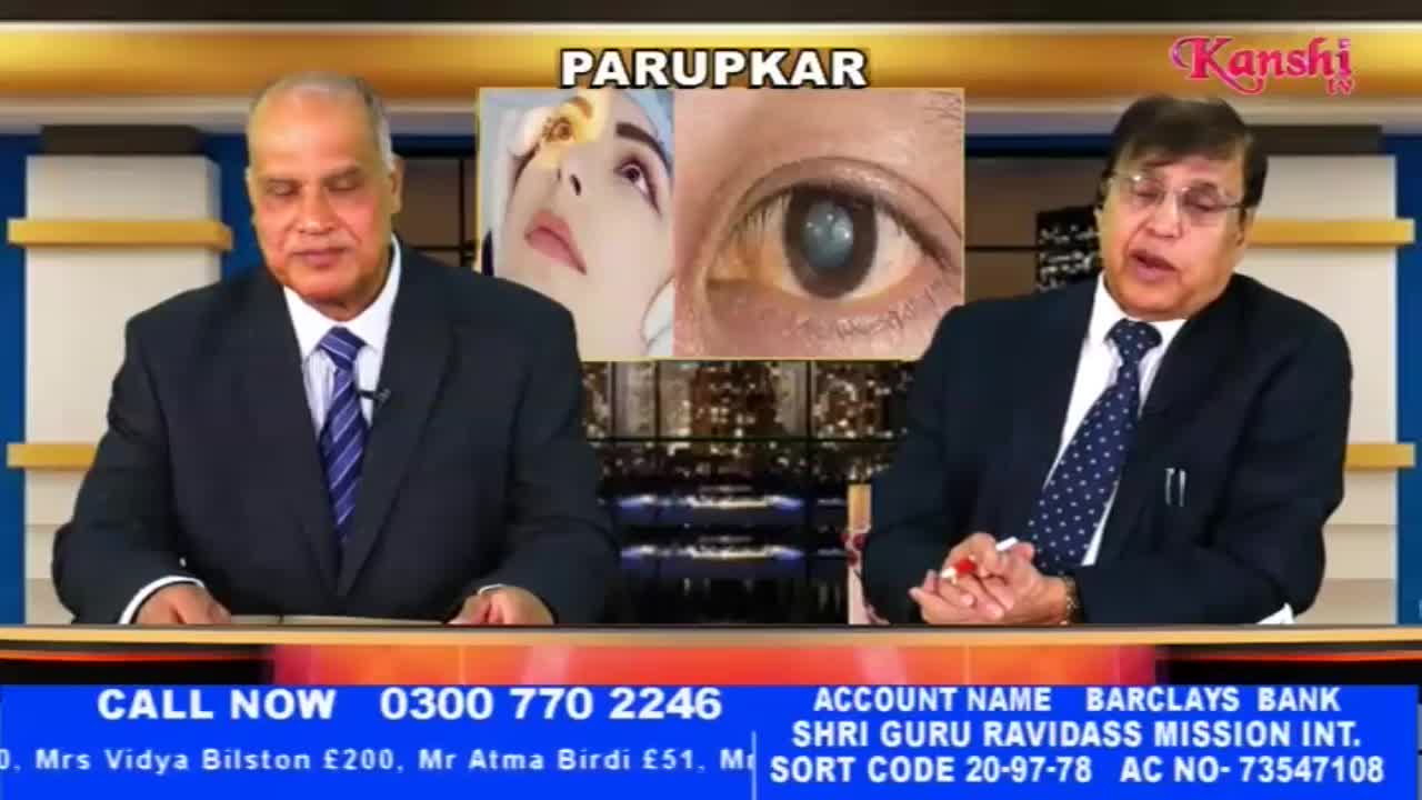 Two men in suits sit at a desk, discussing what appears to be medical information. A split screen behind them shows a close-up of an eye and a woman's face.