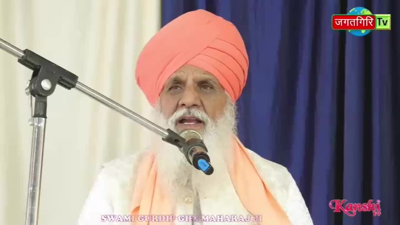 A man in an orange turban speaks into a microphone. A logo for Kanshi TV appears in the corner.