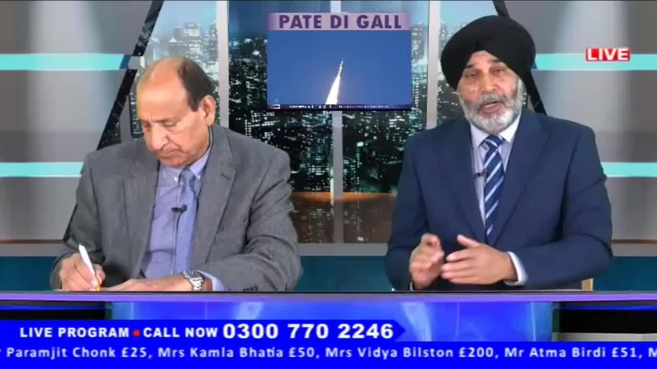 The man on the left is writing on a notepad while the man on the right gestures with his hands. A screen behind them displays a rocket launch.