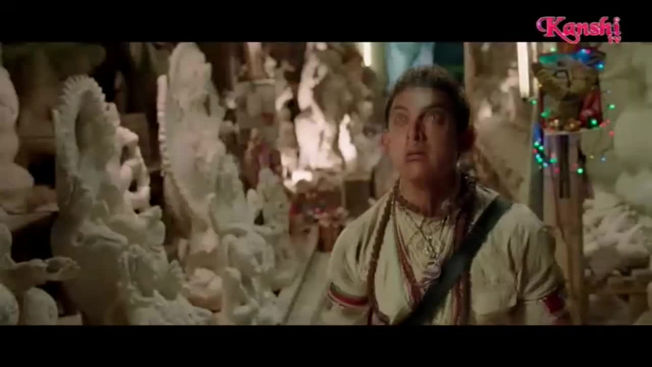 A man with wide eyes stands amidst rows of white statues, looking upwards. Tiny, colorful lights twinkle on a pole to his right.