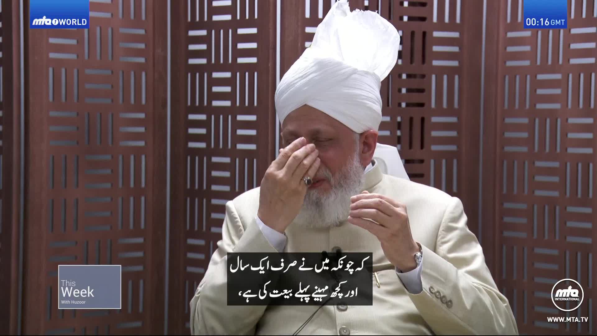 He's seated, wearing a turban and a light-colored suit, with his right hand raised to his face. The man is speaking on MTA1 World, and subtitles appear below him.
