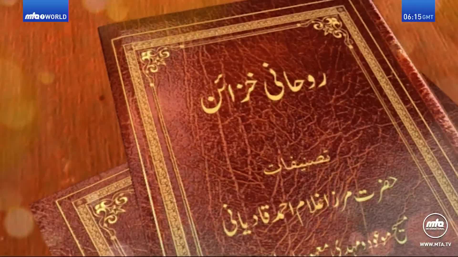 Two leather-bound books rest on a wooden surface, their covers embossed with gold lettering in a foreign script. The MTA World logo is visible in the corner, and the time is 06:15 GMT.
