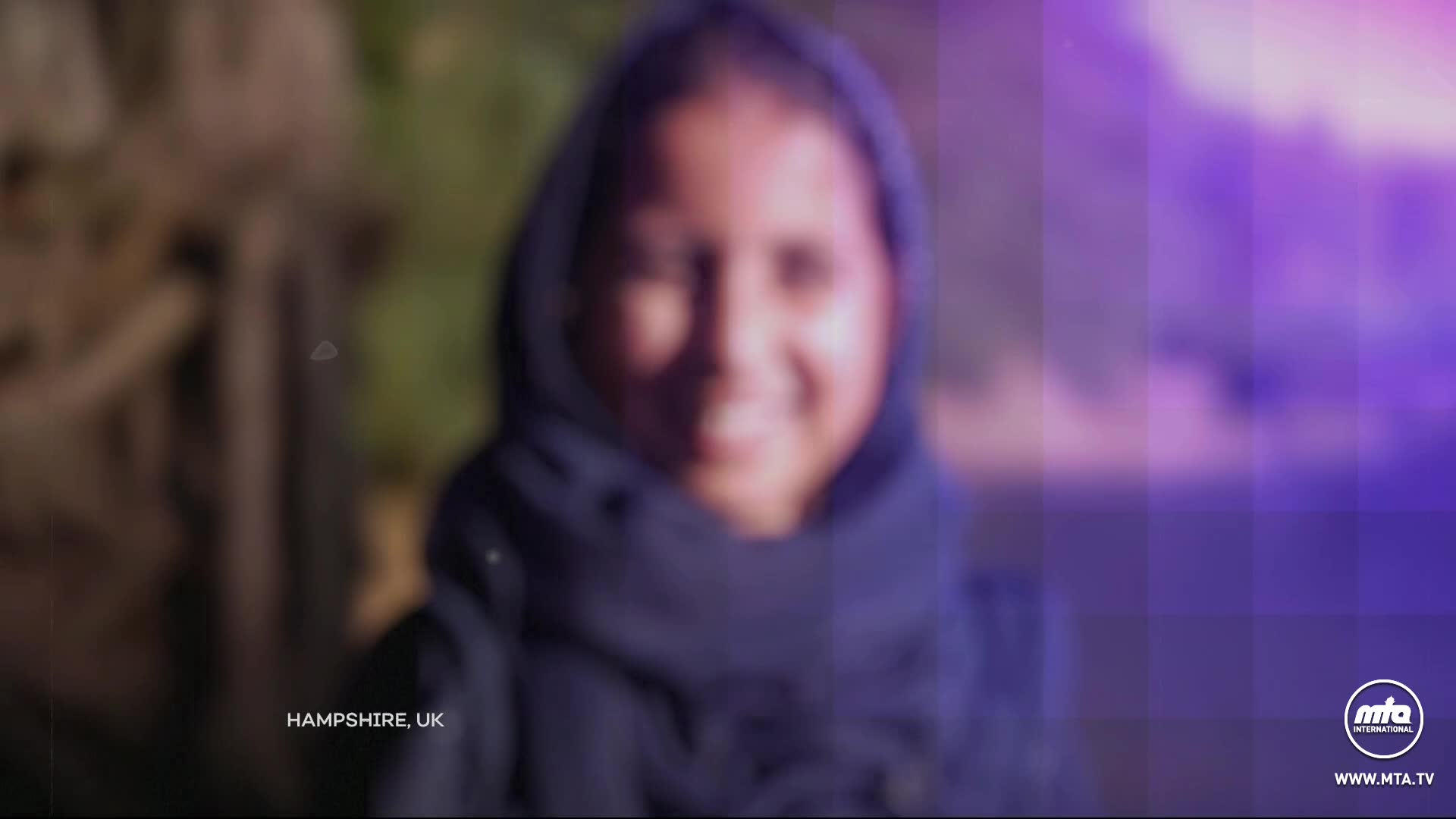 A young person in Hampshire, UK, smiles warmly, their face framed by a dark hood. The MTA1 World logo is visible in the corner.
