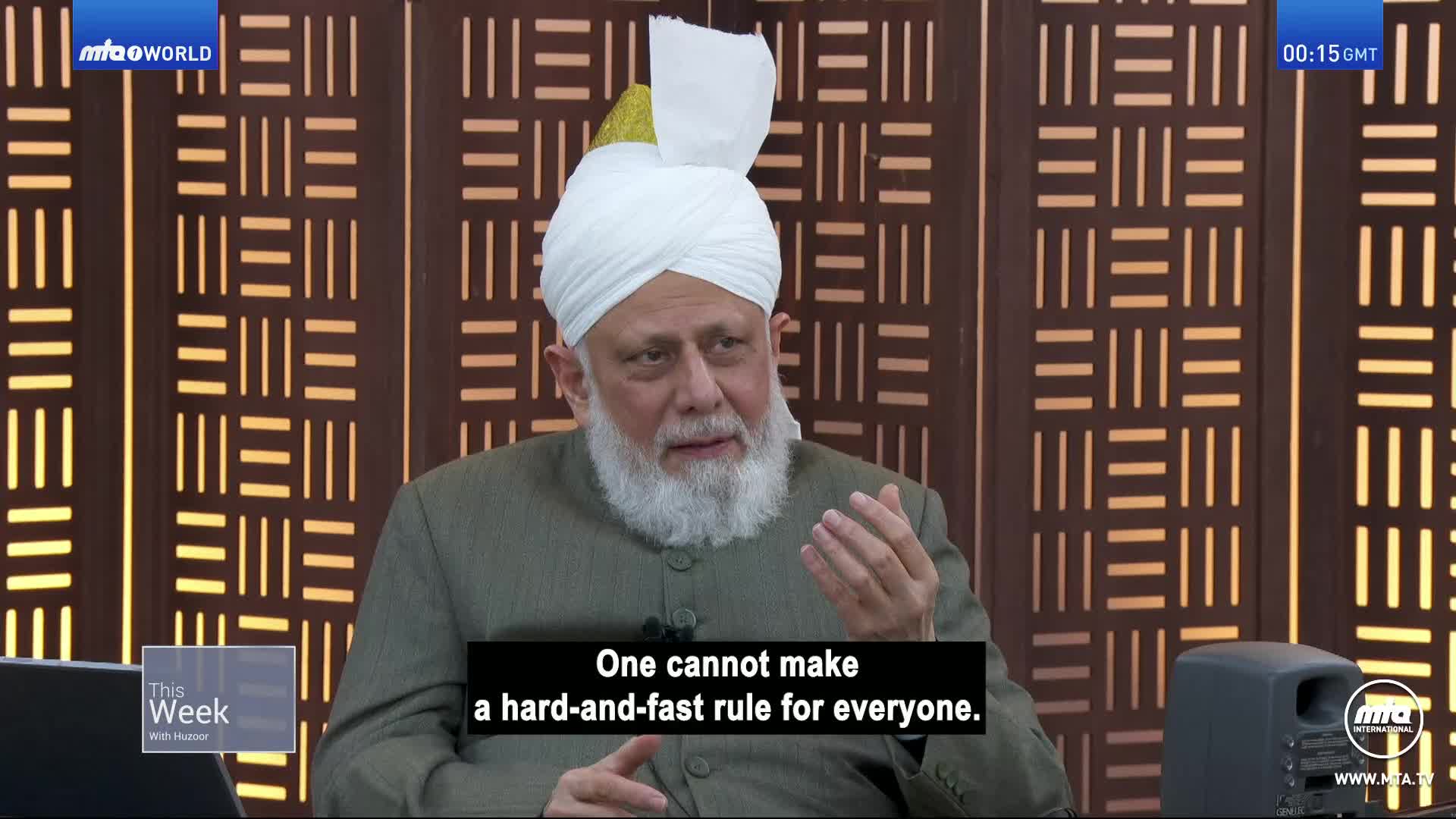 A man in a white turban gestures with his right hand as he speaks, the words "One cannot make a hard-and-fast rule for everyone" appearing on screen. The MTA1 World logo is visible in the corner, and the background is a patterned wooden wall.
