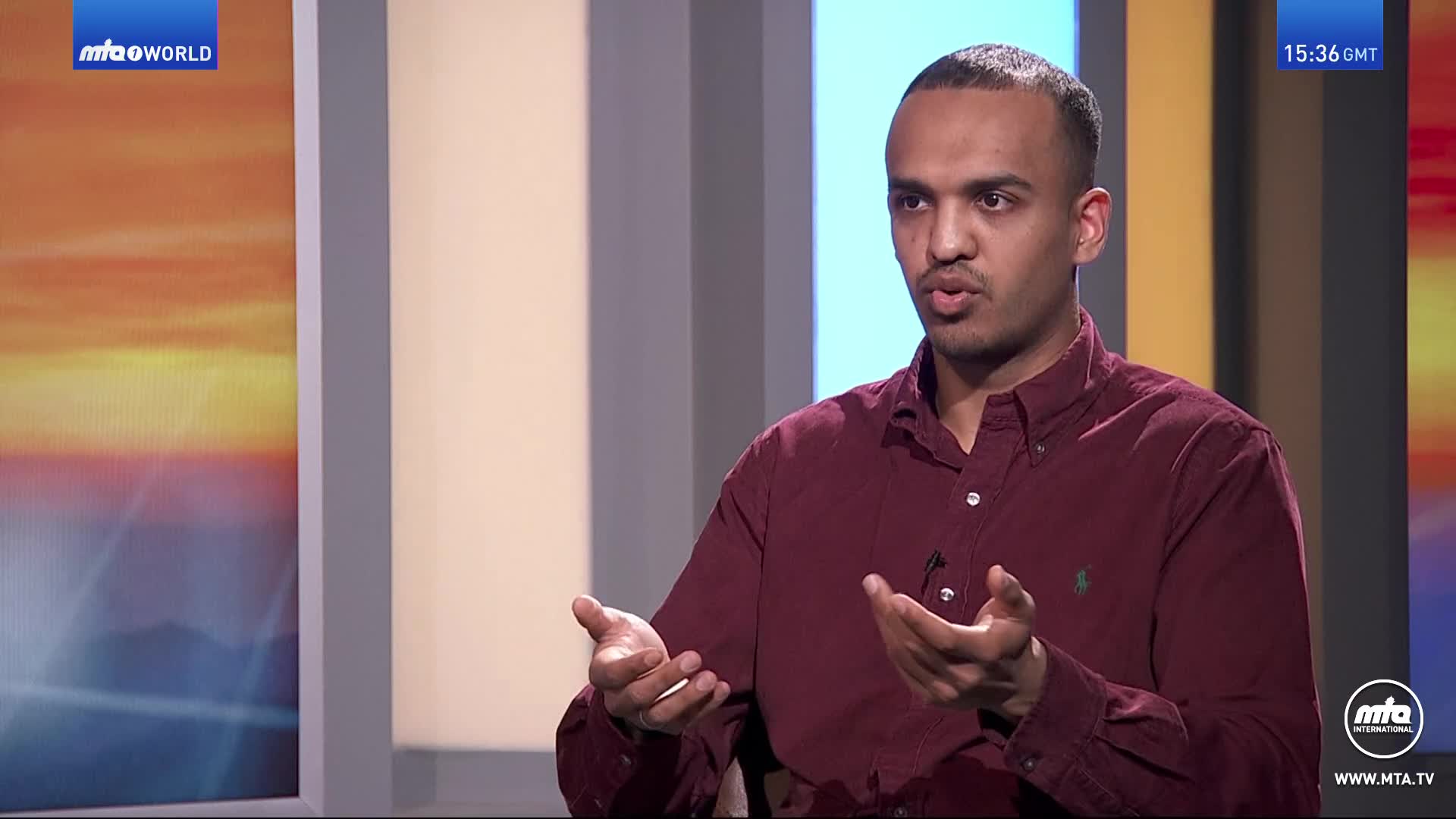 A man in a maroon shirt gestures with his hands while speaking. The MTA World logo appears in the upper left corner. A man in a maroon shirt gestures with his hands while speaking. The MTA World logo appears in the upper left corner.
