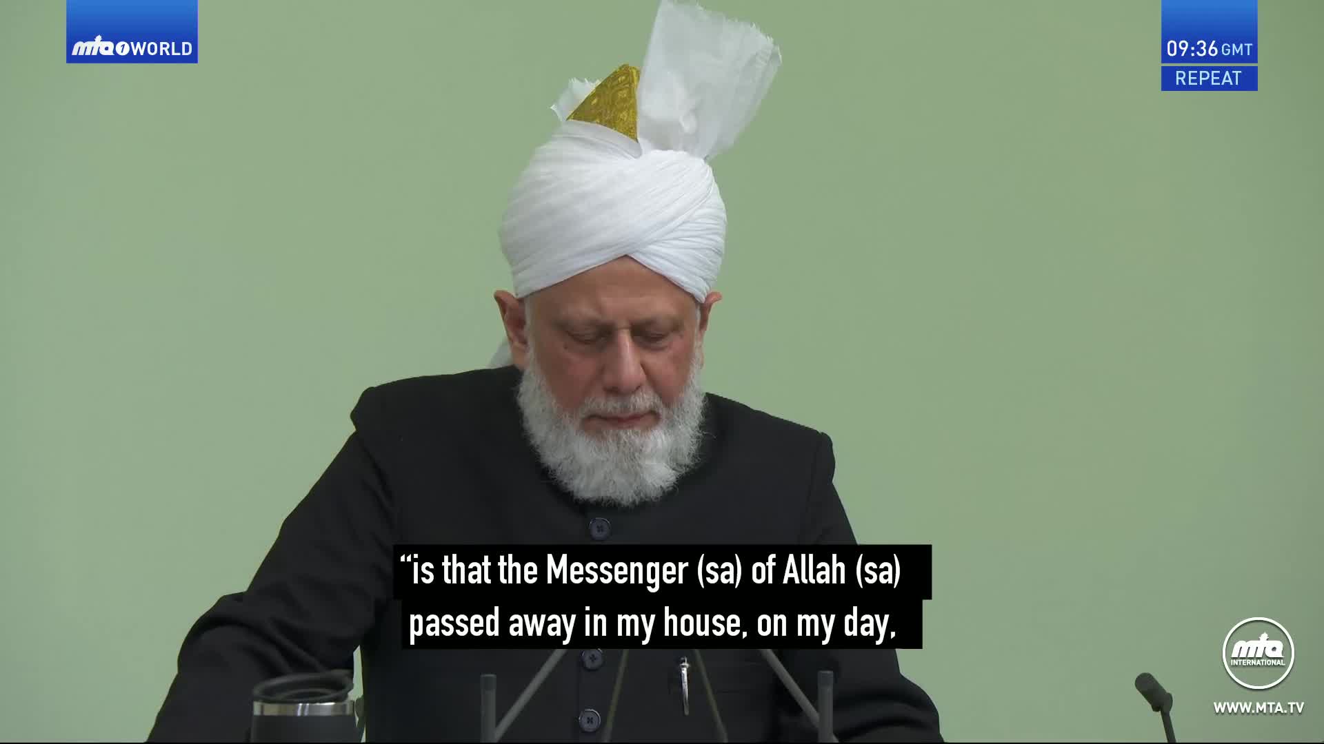 A man with a white turban and beard speaks into a microphone. His words appear on screen, subtitled as a quote from MTA World. A man with a white turban and beard speaks into a microphone. His words appear on screen, subtitled as a quote from MTA World.