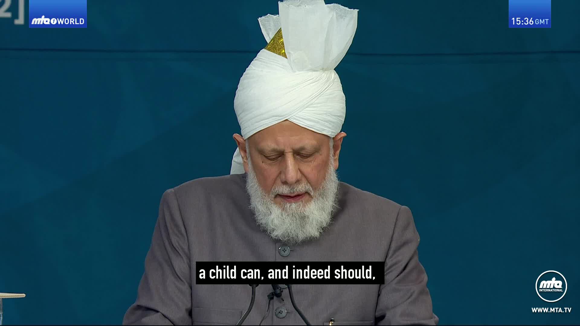 A man with a white turban and a long beard speaks into a microphone. He wears a grey jacket over a white shirt. The MTA World logo appears in the top left corner. A man with a white turban and a long beard speaks into a microphone. He wears a grey jacket over a white shirt. The MTA World logo appears in the top left corner.