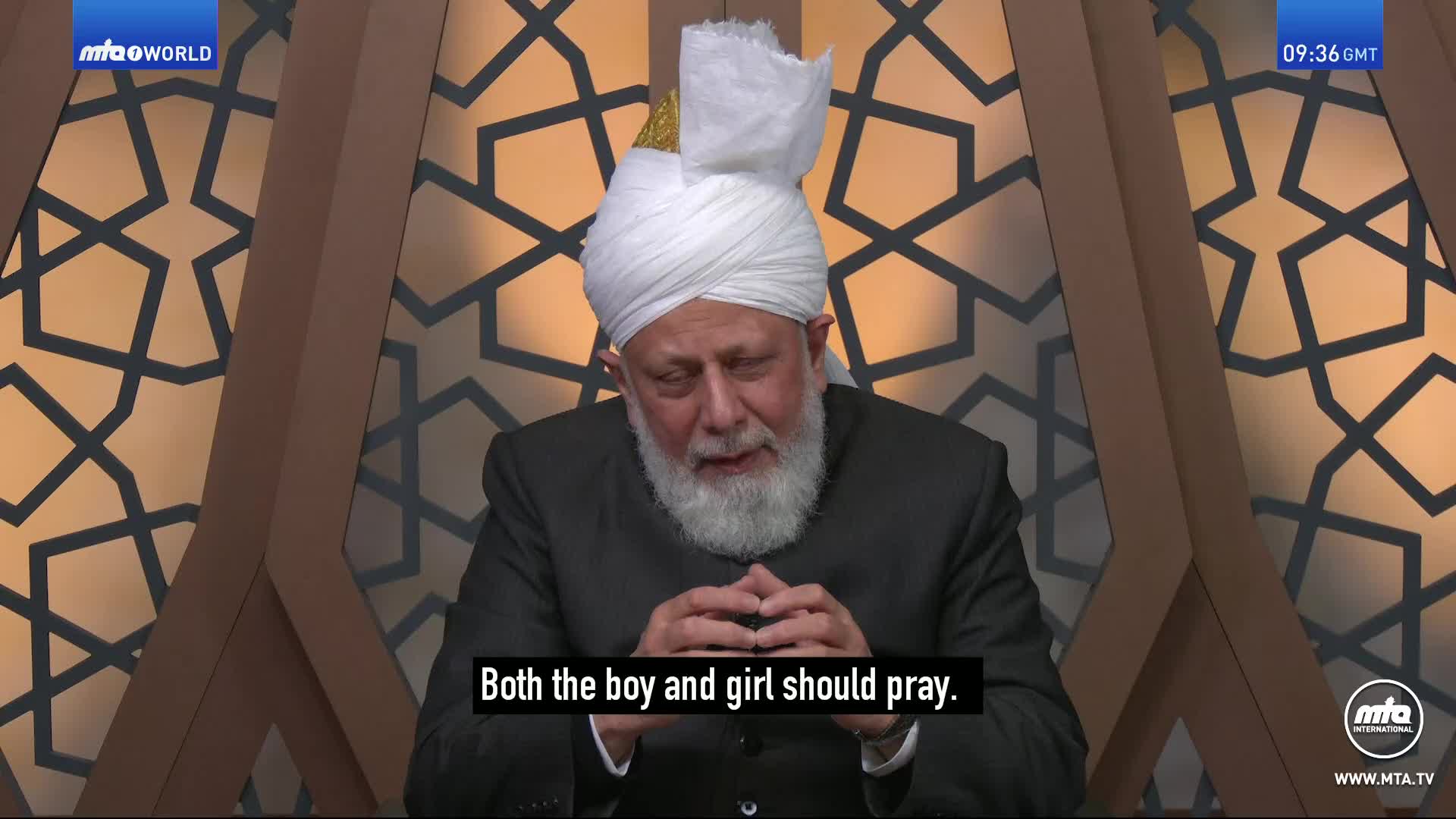 A man in a white turban and dark suit speaks, his hands clasped. The screen displays "MTA WORLD" and the time "09:36 GMT." A man in a white turban and dark suit speaks, his hands clasped. The screen displays "MTA WORLD" and the time "09:36 GMT."