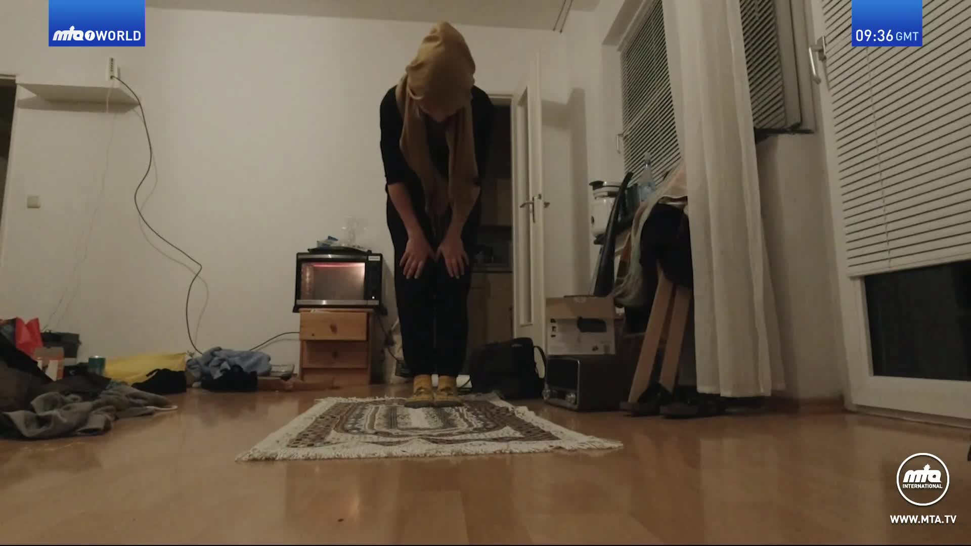 A person in a headscarf is bowing on a rug. The time on the screen reads 09:36 GMT.