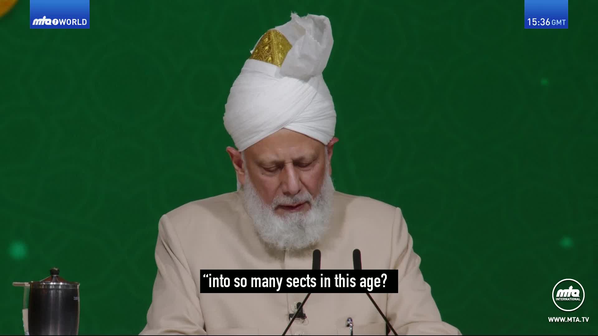 A man in a white turban and beige jacket speaks at a podium. His words, "into so many sects in this age?", are displayed on screen.