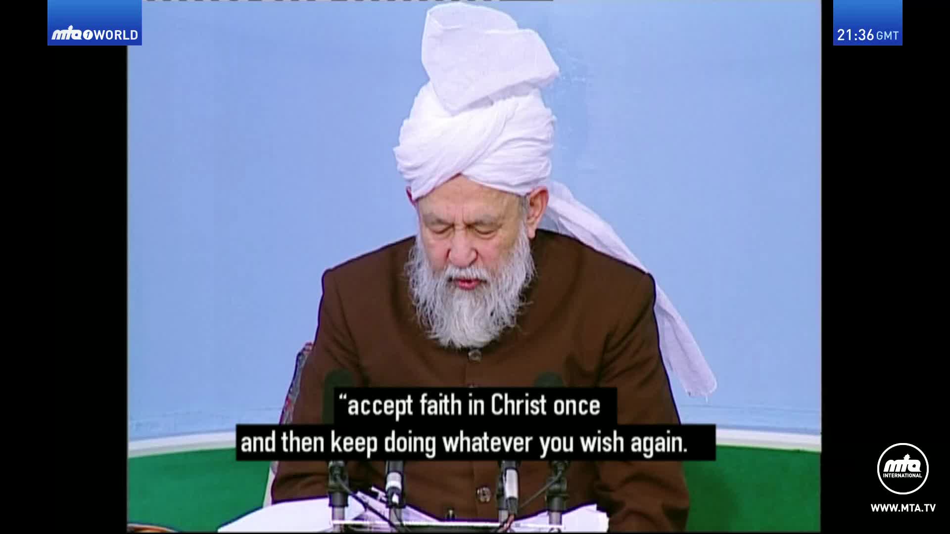 A man with a long white beard, wearing a brown jacket and a white turban, speaks into a microphone. Subtitles below him read, "accept faith in Christ once and then keep doing whatever you wish again."
