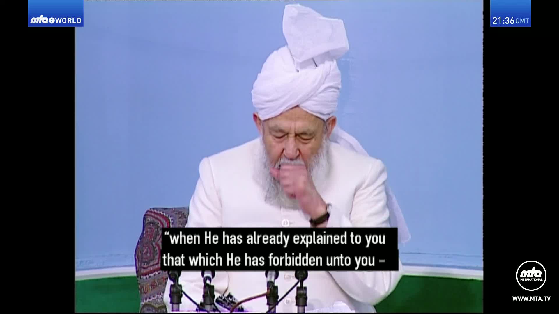 The man in the white turban coughs into his hand. On the screen, the MTA World logo is visible in the top left corner.