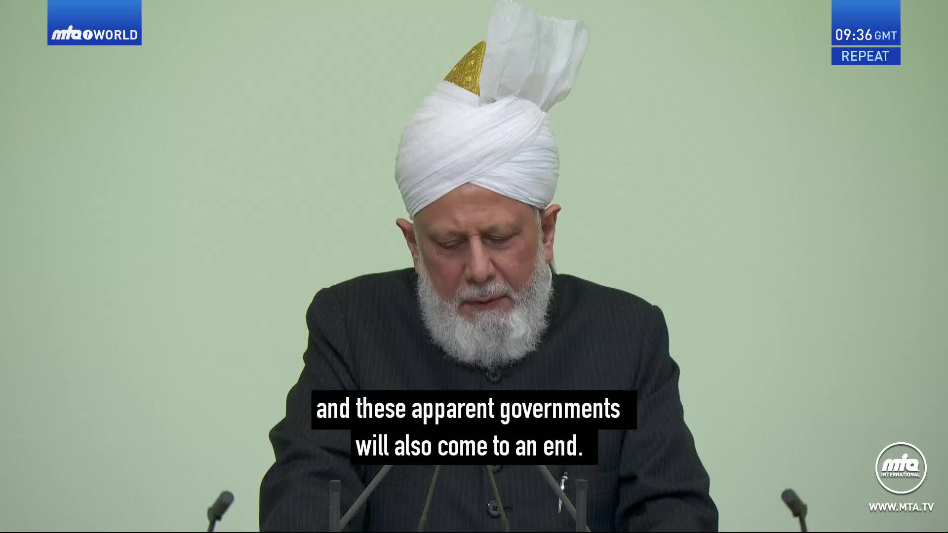 A man in a white turban and dark suit speaks at a podium. The MTA World logo appears in the top left corner.