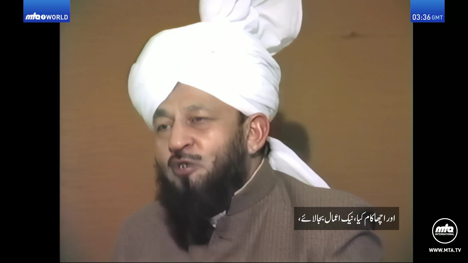 A man in a white turban and brown jacket speaks directly to the camera. Text in Arabic appears on the screen, and a clock in the upper right corner reads "03:36 GMT."