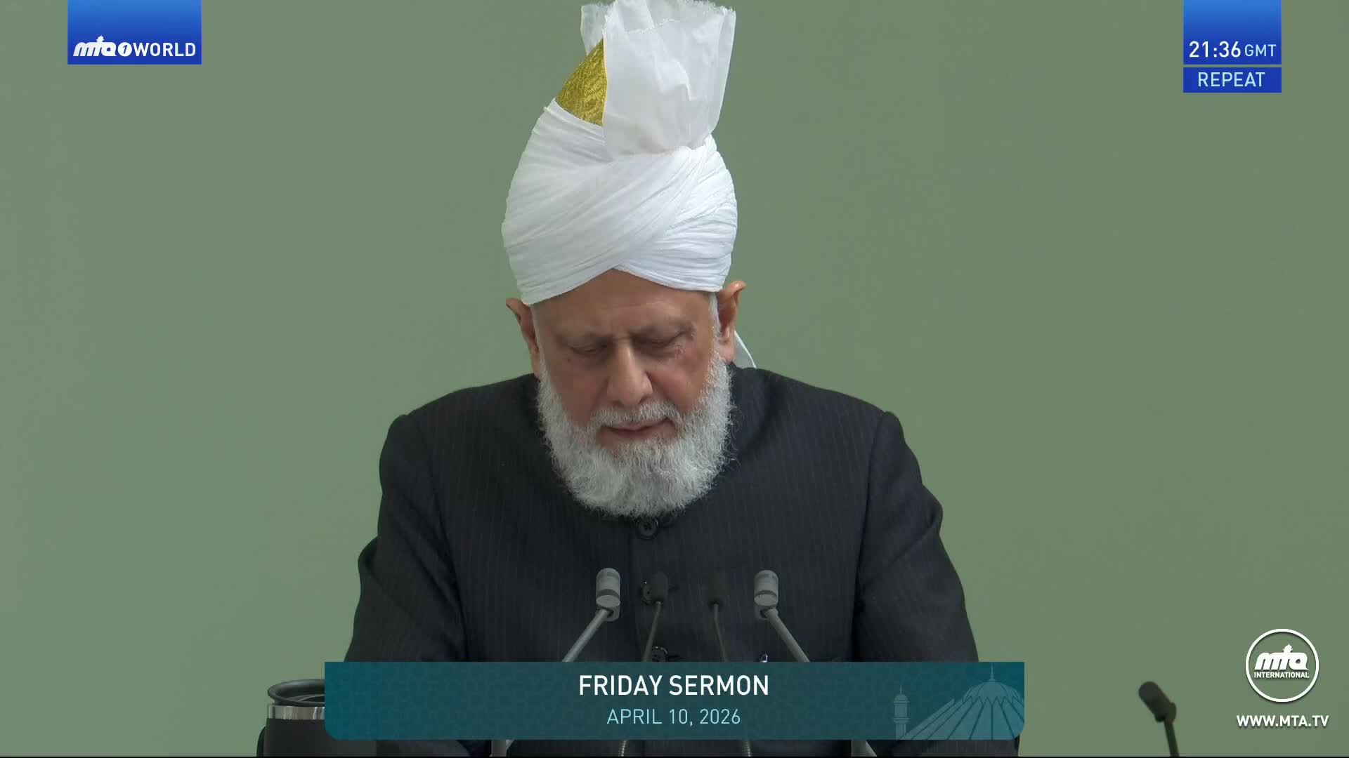 A man in a white turban and dark suit stands at a podium, his head bowed. The screen displays "FRIDAY SERMON APRIL 10, 2026" at the bottom.
