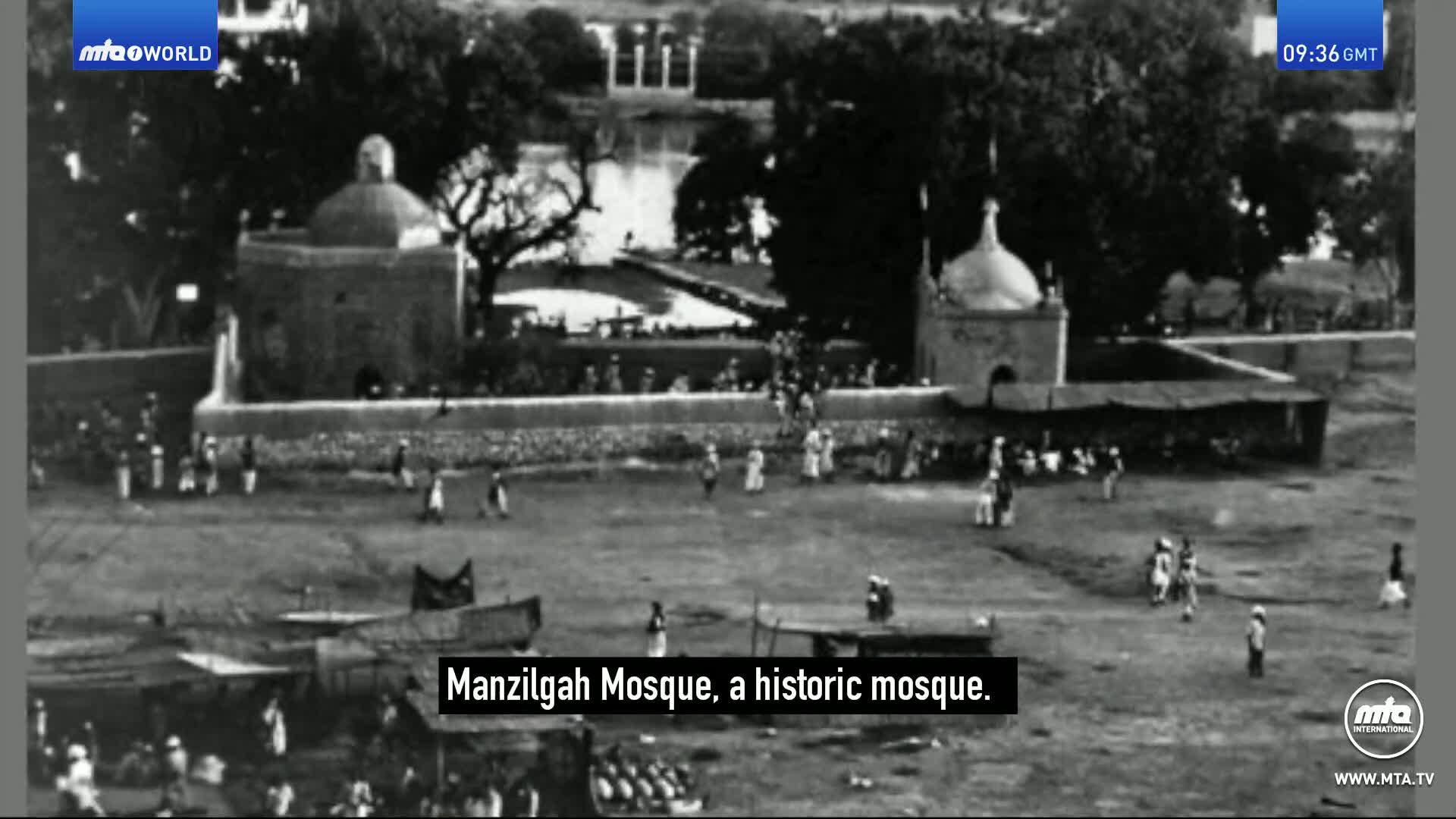 People mill about in the open space before the Manzilgah Mosque, a historic structure. A few figures walk towards the mosque's entrance, while others gather near stalls.