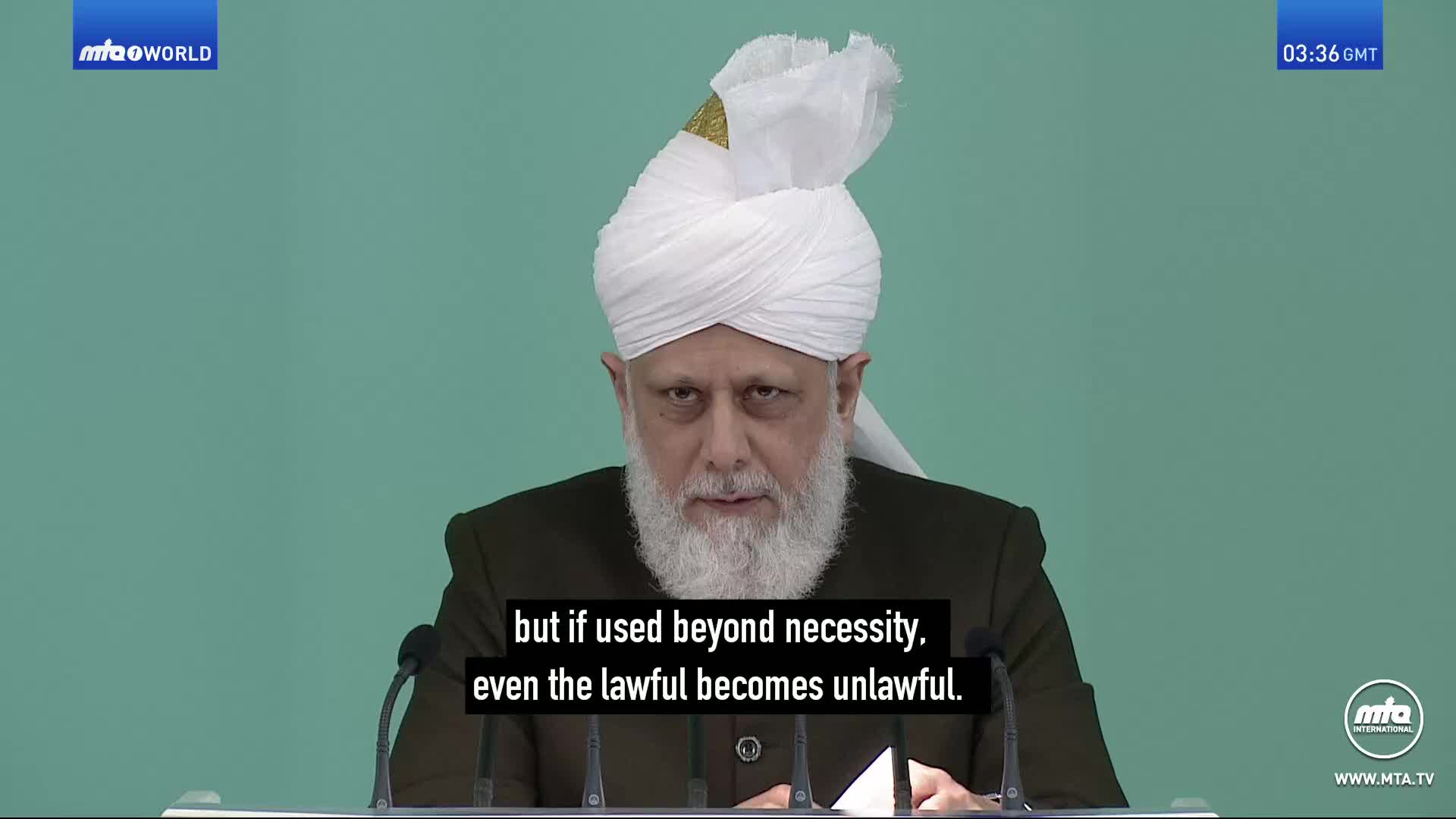 A man in a white turban and dark jacket speaks from behind a podium. The screen displays "MTA World" in the top left corner and "03:36 GMT" in the top right.