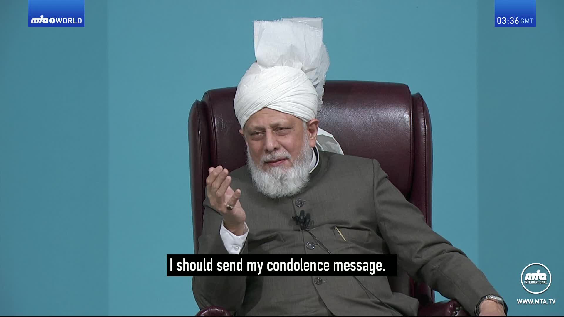 A man in a white turban and a brown suit speaks, his right hand gesturing. Subtitles beneath him read, "I should send my condolence message."