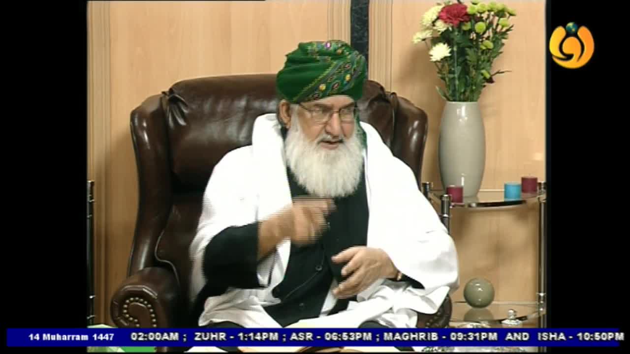 A man with a long white beard and a green turban gestures with his right hand as he speaks. He's seated in a large leather chair, presumably on a Noor TV broadcast from the United Kingdom.
