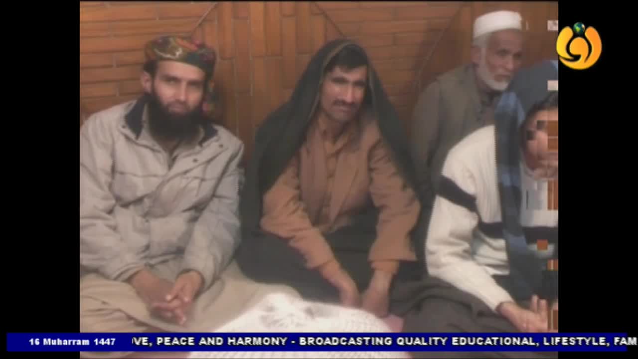 Several men are seated, looking toward the camera, with a Noor TV logo visible in the corner. The man in the center wears a head covering and a brown shirt, while the others are dressed in various jackets and sweaters.
