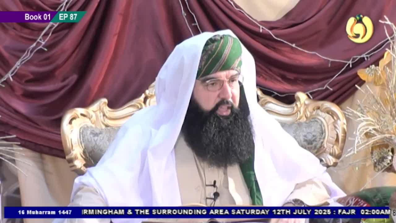 A man with a long, dark beard and a white turban is seated on an ornate chair, speaking into a microphone. The broadcast is from the United Kingdom on Noor TV, with text at the bottom indicating the date and time.
