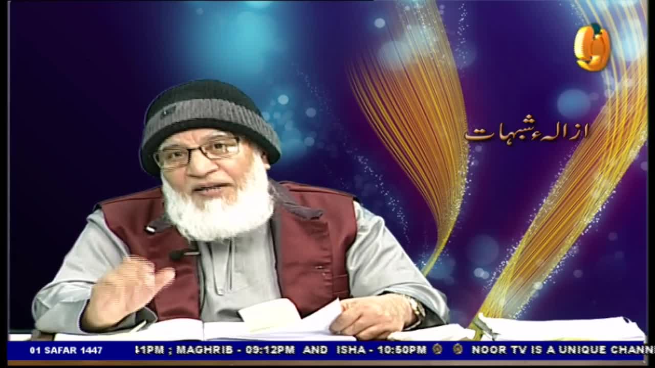 A man with a long white beard and glasses gestures with his right hand, speaking into a camera. Behind him, a Noor TV graphic displays text in Arabic.
