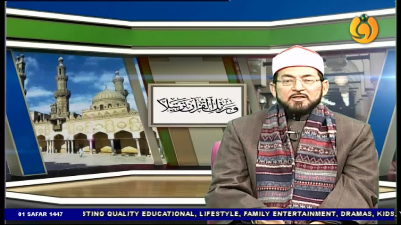 A man in a white cap and patterned scarf sits in a studio, speaking. Behind him, a framed Arabic inscription and a backdrop of a mosque are visible.
