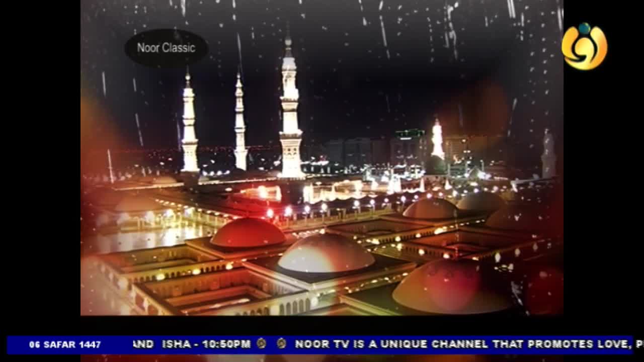 Rain falls over a brightly lit mosque, its minarets piercing the night sky. The scene, broadcast by Noor TV, shows a detailed view of the building's domes and surrounding structures.
