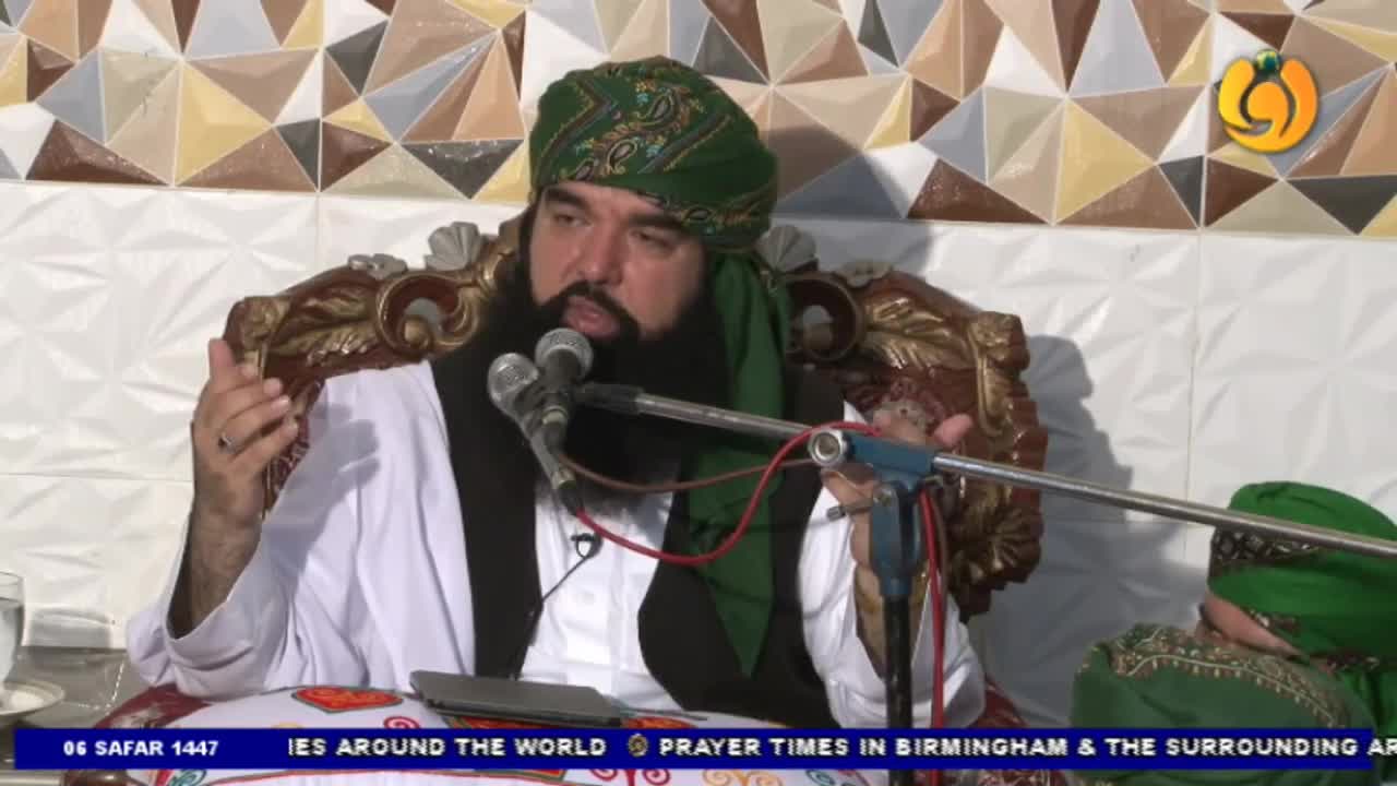A man in a turban speaks into two microphones, his hands gesturing as he talks. The Noor TV logo is visible in the corner, and the broadcast appears to be about prayer times in Birmingham.
