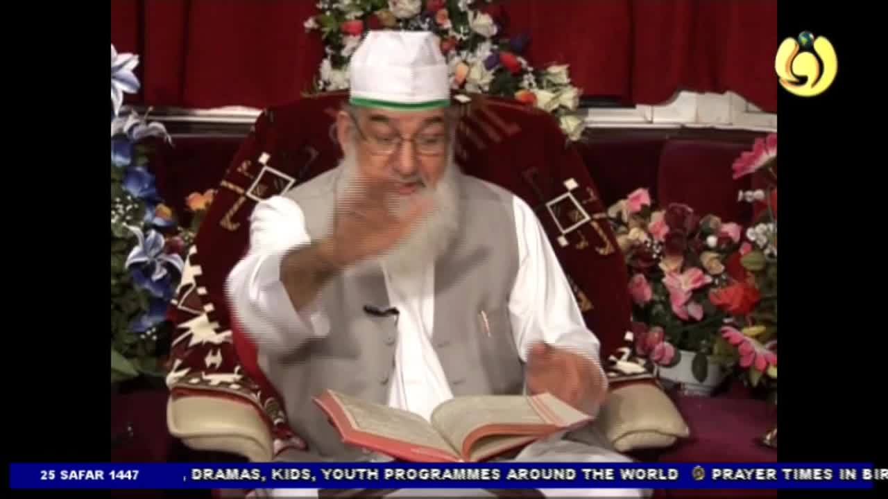 A man in a white cap and vest gestures with his right hand while reading from an open book. He's seated on a patterned chair, with Noor TV's logo visible in the corner.
