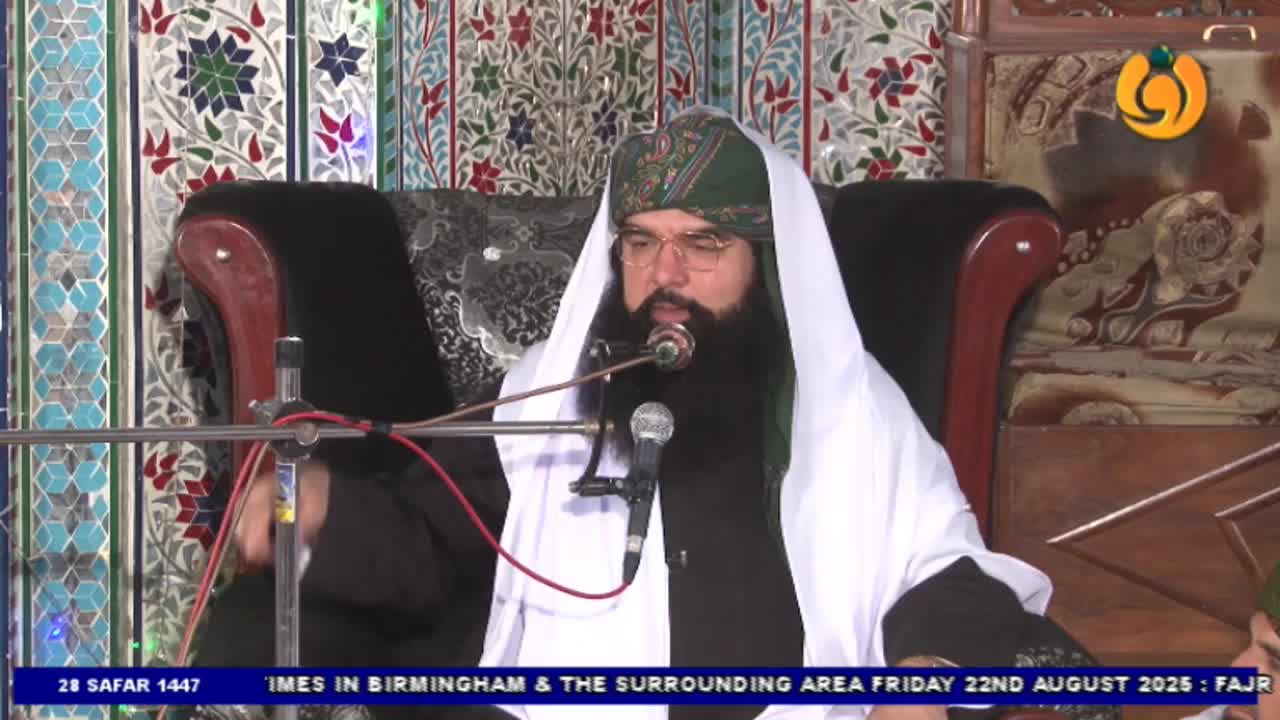 A man with a long black beard and a green turban speaks into a microphone. He's seated in a large, ornate chair, and the Noor TV logo is visible in the corner of the screen.
