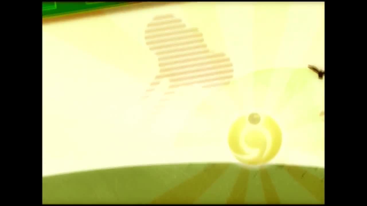 A bright yellow sphere, with a smaller sphere on top, rolls across a green field. Behind it, a light-colored shape and rays of light are visible against a pale yellow background.
