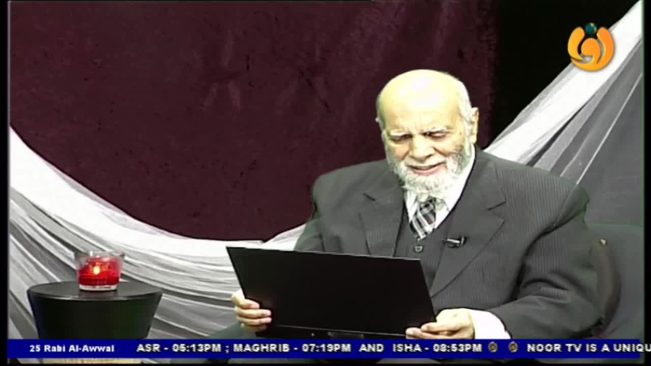 An older man in a suit sits, focused, holding a laptop. A small candle burns on a side table, and the Noor TV logo is visible in the corner.
