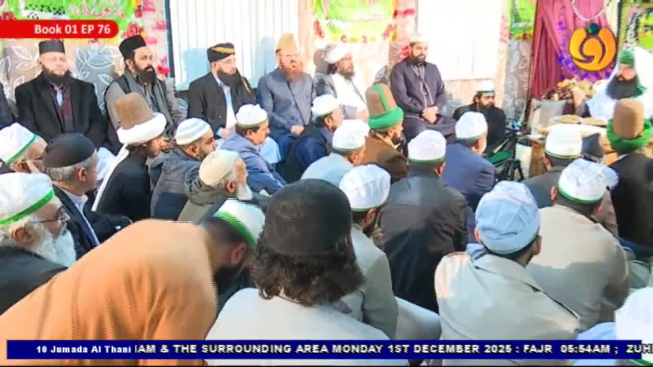 Men in white and green caps sit close together on the floor, listening intently. A group of men with beards and turbans are seated on a raised platform behind them.
