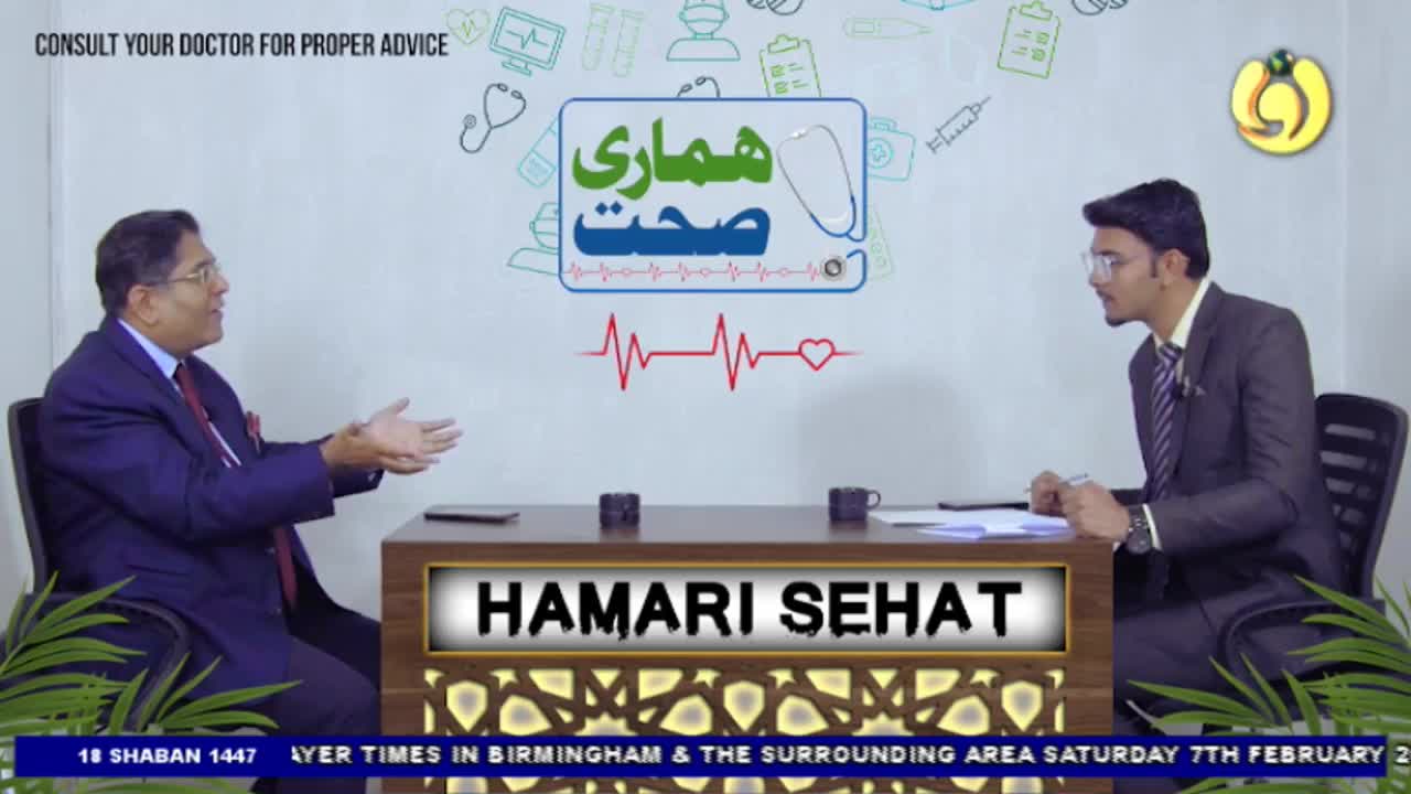 A man in a suit gestures with his hands while speaking to another man across a desk. The Noor TV logo is visible in the background, alongside graphics related to health.