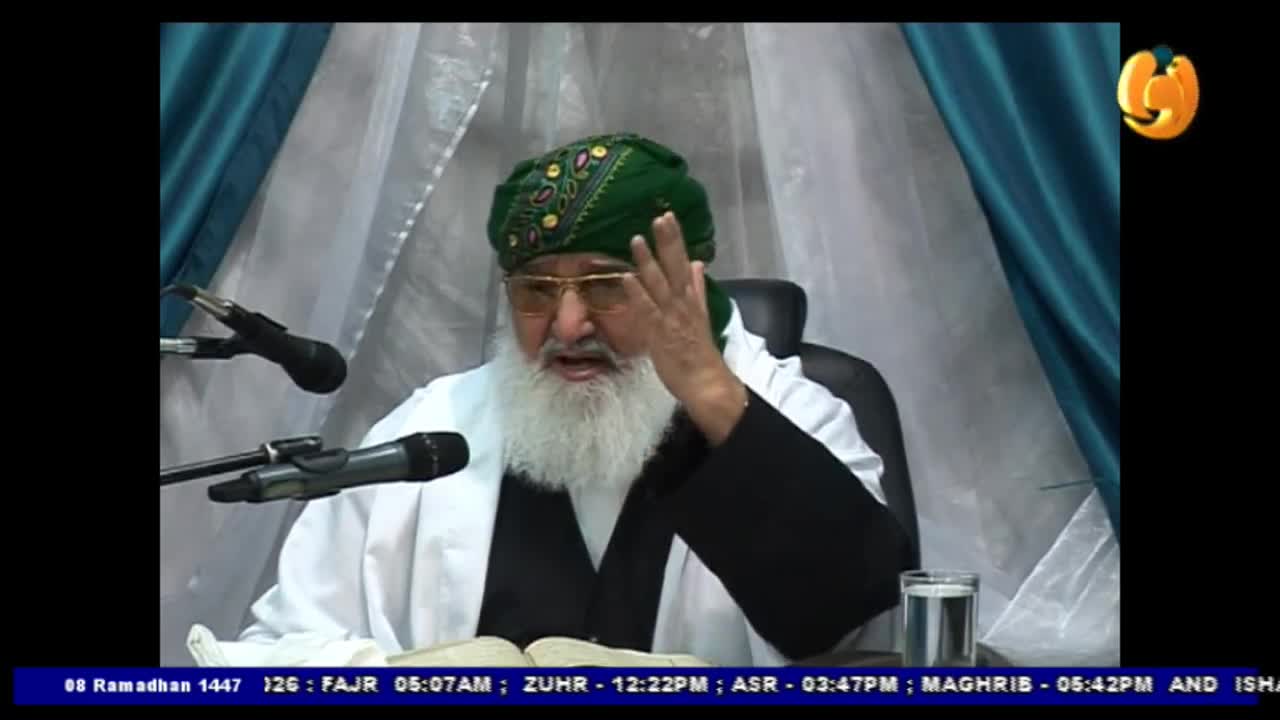 An older man with a long white beard and a green turban gestures with his right hand while speaking. He sits behind a book, with microphones positioned in front of him, likely for a broadcast on Noor TV. An older man with a long white beard and a green turban gestures with his right hand while speaking. He sits behind a book, with microphones positioned in front of him, likely for a broadcast on Noor TV.