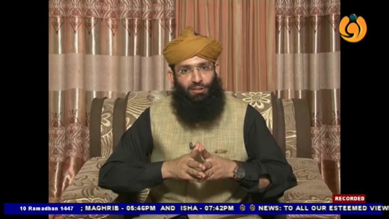 A man with a beard and a turban is speaking, his hands clasped. He sits on a patterned sofa in front of a curtained wall, a small logo in the corner of the screen. A man with a beard and a turban is speaking, his hands clasped. He sits on a patterned sofa in front of a curtained wall, a small logo in the corner of the screen.
