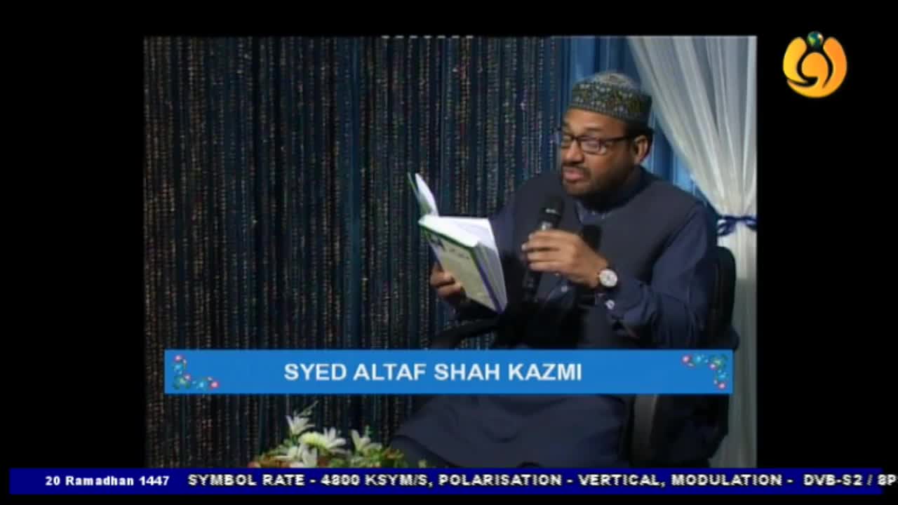 A man in a cap and glasses holds a book open, speaking into a microphone on a stage. The Noor TV logo is visible in the upper right corner.