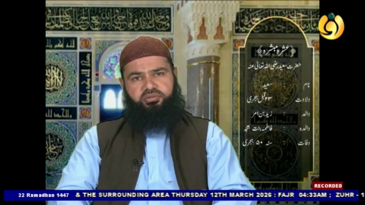 A man with a beard and a maroon cap speaks directly to the camera. Behind him, Arabic calligraphy adorns the walls of what appears to be a mosque.